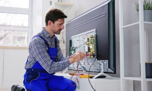 Young Male Electrician In Overall Checking Television